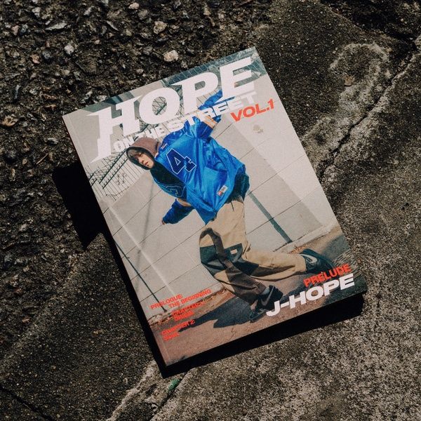 imagen del disco Hope on the Street Vol. 1 de J-Hope, donde se ve una portada de una revista tirada en el suelo de una calle. La revista tiene en la portada una foto con J-Hope bailando,